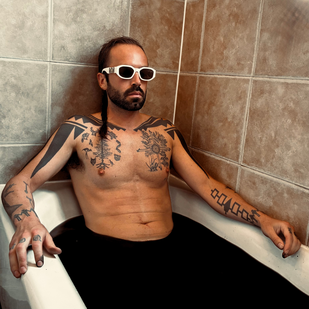 OPLIAM seated in a bathtub wearing sunglasses