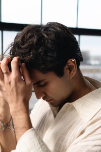 Sid Seth bows his head with his hands resting against his forehead beside a window.
