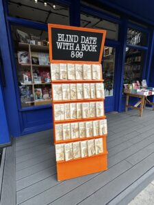 An orange stand of wrapped books outside Camden Town Bookshop's blue storefront.