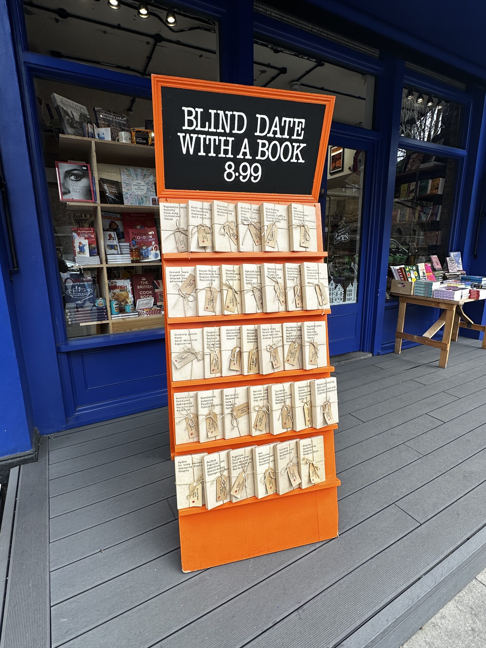 An orange stand of wrapped books outside Camden Town Bookshop's blue storefront.