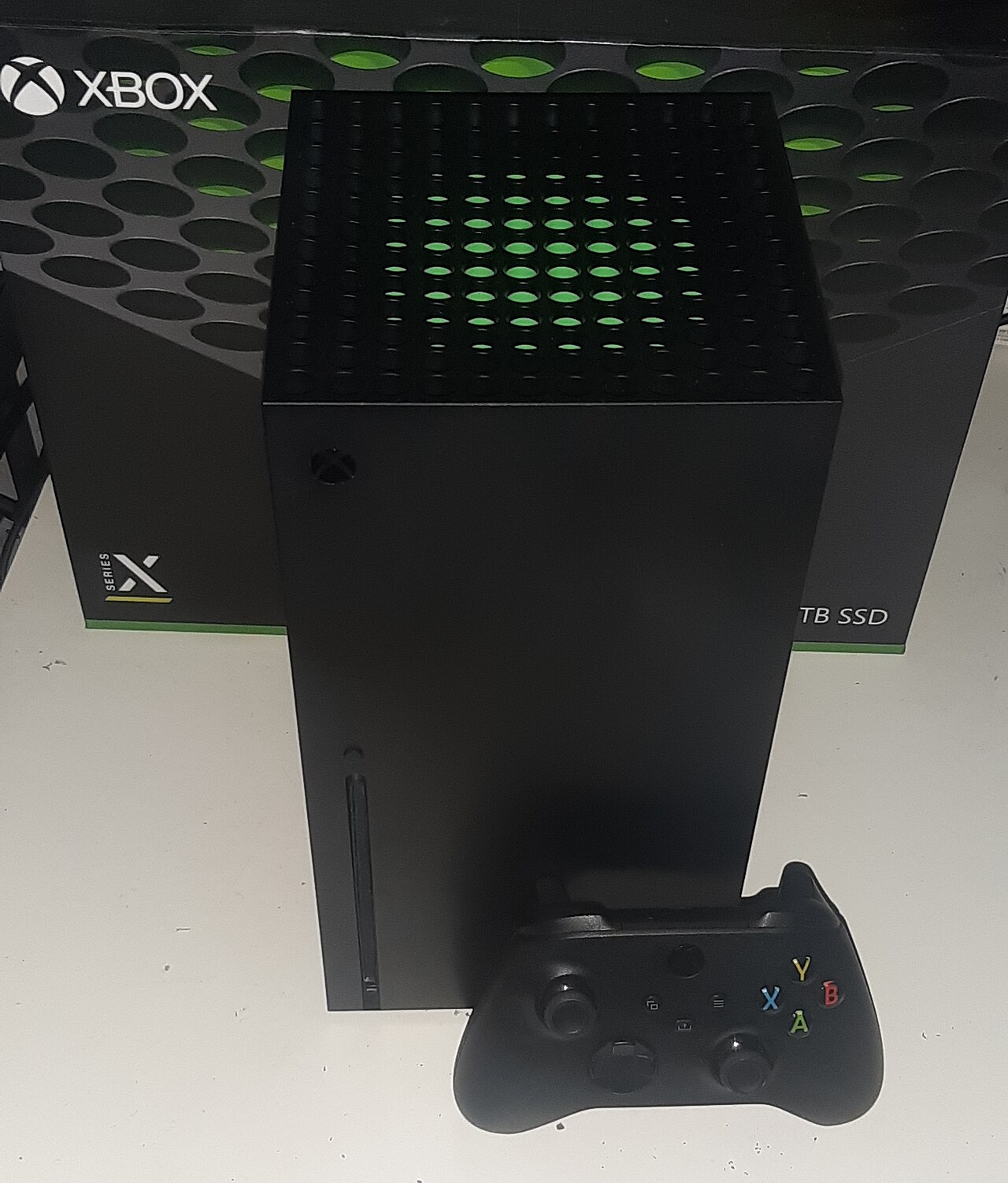 A black Xbox Series X console and controller in front of the console's retail box.
