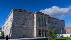 The National Gallery of Ireland's stone entrance façade with visitors outside and an Irish flag.