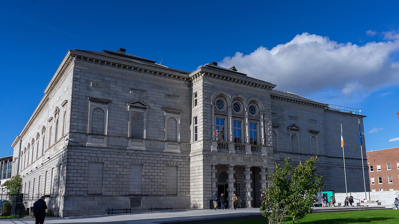 The National Gallery of Ireland's stone entrance façade with visitors outside and an Irish flag.