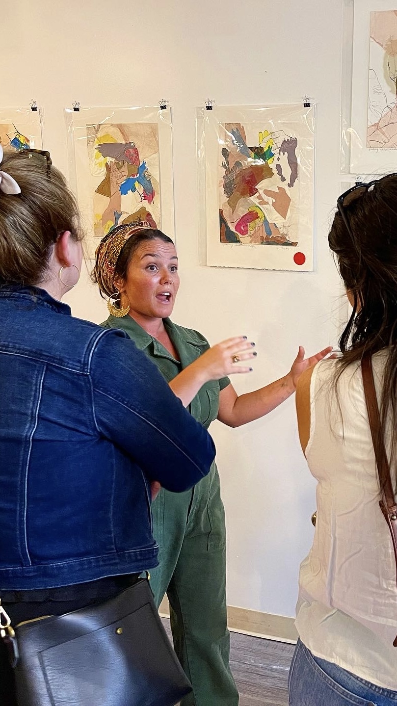 Eileen Brodaski speaks with visitors in front of colorful hand prints at her Thumb Wars exhibition.