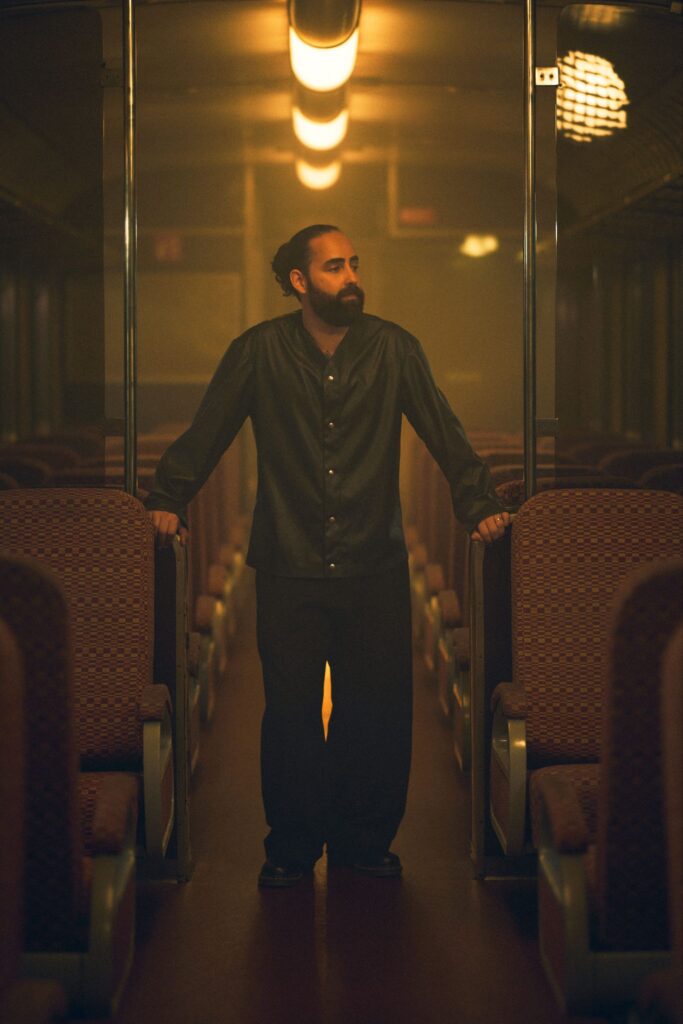 J.MYSTERY standing between seats inside a train carriage.