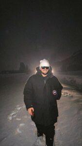Karim Panzetta wearing a winter coat, knit hat and sunglasses outdoors in the snow at night.