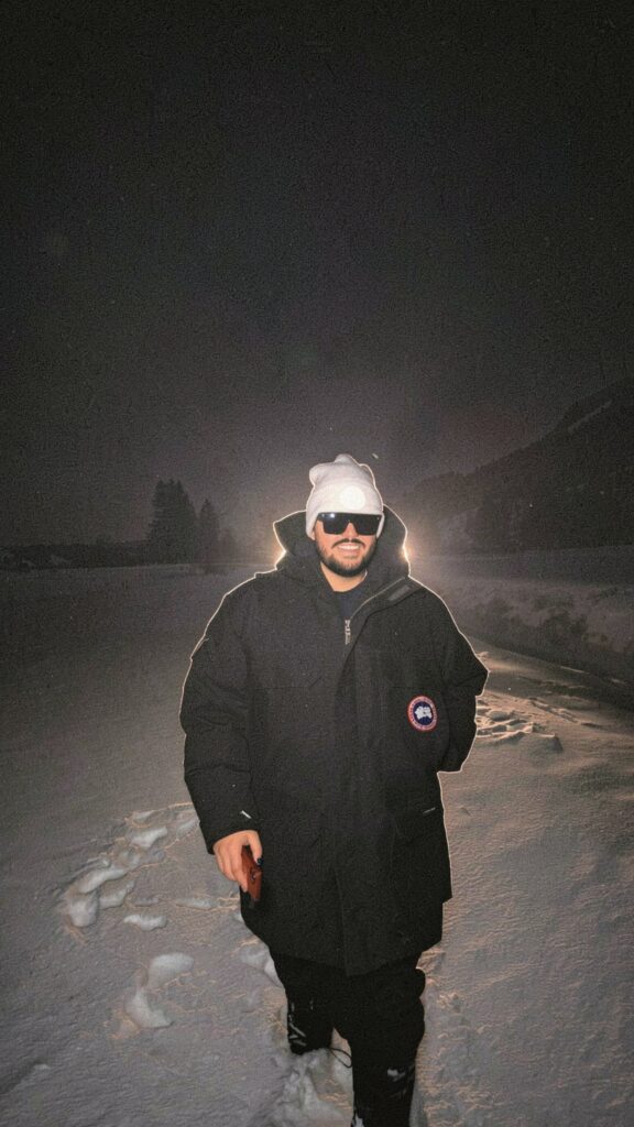 Karim Panzetta wearing a winter coat, knit hat and sunglasses outdoors in the snow at night.