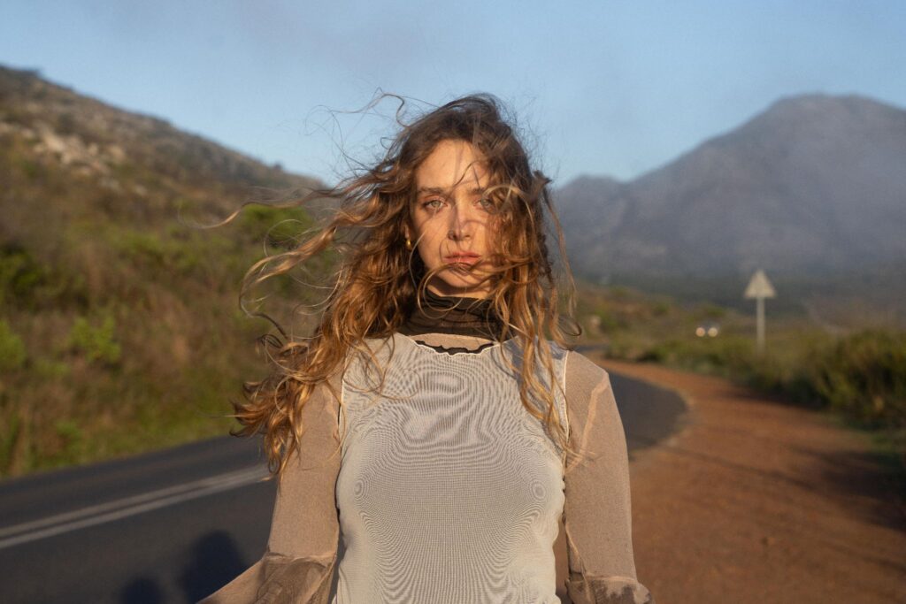 Manu Grace stands on a road with mountains behind her in a promotional portrait.