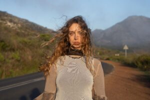 Manu Grace stands on a road with mountains behind her in a promotional portrait.