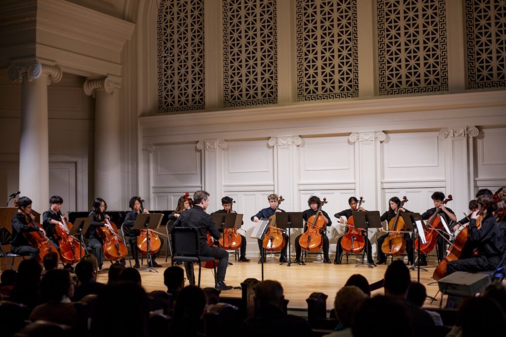 The Suzuki Cello Ensemble performs with a conductor on the Nichols Concert Hall stage.