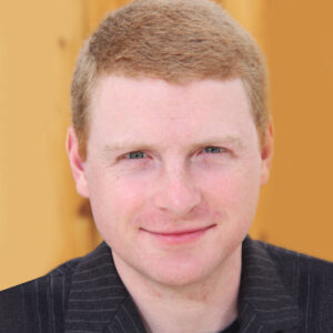 Portrait of George Cederquist wearing a dark blazer against a yellow background.