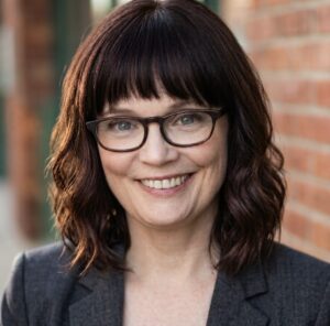 Headshot of Abby McEntee, wearing glasses and a dark blazer.